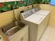 Laundry room with updated washer, dryer, utility sink, cabinets, and tropical themed wallpaper at 213 Bayside Ct, Nokomis, FL 34275