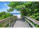A serene view of a sandy path to the beach framed by lush greenery and a wooden boardwalk at 471 Bayshore Rd, Nokomis, FL 34275