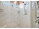 Detailed shot of shower with marble-like tile walls, rain shower head, and glass door, and built-in shelves at 632 Valencia Rd, Venice, FL 34285