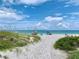 Sandy path leading to a scenic beach with clear blue water, umbrellas, and people enjoying the sunny day at 8603 46Th Avenue W Cir, Bradenton, FL 34210