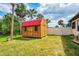 Outdoor storage shed with a red roof and wooden construction surrounded by lush green grass and tropical landscaping in the backyard at 9407 Prospect Ave, Englewood, FL 34224