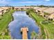 Aerial view of a pond with a dock surrounded by lush lawns and well-maintained community buildings at 410 Mission E Trl # H, Venice, FL 34285