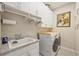 Well-lit laundry room featuring granite counters, storage cabinets, utility sink, and modern washer and dryer at 24036 Spartina Dr, Venice, FL 34293