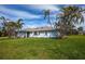 Charming light blue home featuring a lush lawn and tropical landscaping with palm trees against a blue sky at 8170 Casa De Meadows Dr, Englewood, FL 34224