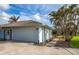 Garage featuring a large white door and a concrete driveway, surrounded by palm trees and a vibrant blue sky at 8170 Casa De Meadows Dr, Englewood, FL 34224