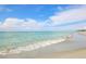 Calm ocean waves gently washing onto a white sandy beach under a clear blue sky with fluffy white clouds at 325 Fiesole St, Venice, FL 34285