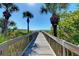 Picturesque wooden boardwalk leading to a sunny beach with clear blue skies and swaying palm trees at 720 Apalachicola Rd # 104, Venice, FL 34285