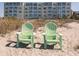 A view of the oceanfront building from the sandy beach featuring two green Adirondack chairs at 950 Tarpon Center Dr # 506, Venice, FL 34285