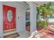 Welcoming red front door with decorative glass, enhanced by stone accents and tropical landscaping at 1048 Ulrey Ln, Englewood, FL 34223