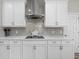 Close-up of the modern kitchen featuring white cabinetry, herringbone backsplash, and stainless steel range hood at 19800 Montenero Way, Venice, FL 34293