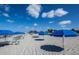 Sandy beach dotted with vibrant blue umbrellas under a clear sky at 6037 Shearwater Dr, Englewood, FL 34224