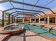 Screened in pool with waterfall feature, hot tub, stone-paver surround, and outdoor kitchen in backyard at 101 Portofino Dr, North Venice, FL 34275