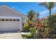 A close exterior view of the garage with well maintained landscaping including flowering bushes and mature palms at 1853 San Silvestro Dr, Venice, FL 34285