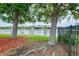Lush backyard with mature trees, green grass, a black metal fence, and tranquil lake views at 20176 Tesoro Dr, Venice, FL 34293