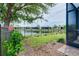 Green backyard featuring a black metal fence, blooming hibiscus, and a peaceful lake backdrop at 20176 Tesoro Dr, Venice, FL 34293