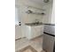Well-lit kitchenette featuring white cabinets, a double stainless sink, open shelving, and tile floors at 2211 Englewood Rd, Englewood, FL 34223