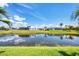 Picturesque view of a well-manicured backyard with a pond, neighboring homes, and vibrant blue sky at 226 W Pine Valley Ln, Rotonda West, FL 33947