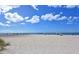 Expansive white sand beach with clear blue water and scattered umbrellas under a partly cloudy sky at 328 Channel Ln, Nokomis, FL 34275