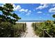 Charming beach path with rope fencing amidst lush greenery, leading to a beautiful beach with clear skies and gentle waves at 328 Channel Ln, Nokomis, FL 34275
