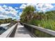 A wooden boardwalk with side railing flanked by palm trees, invites exploration amidst a peaceful tropical setting at 328 Channel Ln, Nokomis, FL 34275