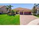 Charming single-story home featuring a red tile roof, brick driveway, and lush landscaping with tropical palm trees at 13897 Umbria St, Venice, FL 34293