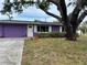 Charming single-story home boasts a bright purple exterior, white trim, and a large tree providing shade at 1460 Everest Rd, Venice, FL 34293
