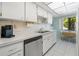 Bright kitchen features white cabinetry, stainless steel dishwasher, and sunlit breakfast nook with tree views at 1555 Tarpon Center Dr # 156, Venice, FL 34285
