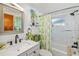 Bright bathroom featuring white marble-style tiling, a modern vanity, and a shower-tub combo with a leafy green curtain at 1585 Keyway Ct, Englewood, FL 34223