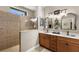 Neutral bathroom featuring a tiled shower with glass partition, sconce lighting above framed mirrors and double sinks at 20479 Pezzana Dr, Venice, FL 34292