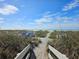 Beach entrance with lush vegetation, beach chairs, and calm ocean waters under a sunny, partly cloudy sky at 500 Park S Blvd # 62, Venice, FL 34285
