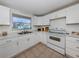 Bright kitchen featuring white cabinetry, white appliances, tile flooring, and a window with backyard views at 504 Buena Vista Dr, Nokomis, FL 34275