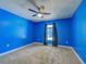 This bedroom features neutral carpeting, a ceiling fan, blue walls and window with black curtains at 14352 Pocono Ave, Port Charlotte, FL 33981