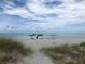 Picturesque beach scene featuring two colorful umbrellas and chairs facing the serene ocean under a cloudy sky at 19893 Cobblestone Cir, Venice, FL 34292