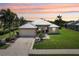 Charming single-story home featuring lush landscaping, a metal roof, and a two-car garage, all under a vibrant sunset sky at 19893 Cobblestone Cir, Venice, FL 34292
