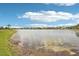 Peaceful water view of a community pond with a grassy bank and sunny blue skies at 19893 Cobblestone Cir, Venice, FL 34292