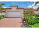 Inviting front exterior with a red brick driveway, two-car garage, and lush tropical landscaping at 24128 Spartina Dr, Venice, FL 34293
