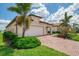 Beautiful exterior with tropical landscaping, a brick driveway, and a spacious two-car garage at 24128 Spartina Dr, Venice, FL 34293