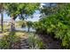 Lakeside backyard featuring lush vegetation and a stone pathway leading to tranquil waterside views, enhanced by mature trees at 442 Sunset Lake Blvd # 104, Venice, FL 34292