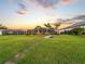 Expansive backyard featuring a screened pool, mature palm trees, and lush green lawn at sunset at 5035 Collingswood Blvd, Port Charlotte, FL 33948