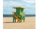 Scenic shot of a vibrant green and yellow lifeguard stand on a sandy beach, set against a backdrop of blue sea and sky at 510 Airport E Ave # 2C, Venice, FL 34285