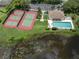 Aerial view showing well-maintained tennis courts, a pool, and clubhouse amidst lush green landscaping and a pond at 615 May Apple Way, Venice, FL 34293