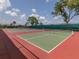 Multiple tennis courts with green surface, red perimeter, and surrounding lush landscaping under a partly cloudy sky at 615 May Apple Way, Venice, FL 34293