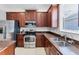 The kitchen features stainless steel appliances, tile floors, and warm wood cabinetry with granite countertops at 2094 Mesic Hammock Way, Venice, FL 34292