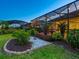 The landscaped backyard showcases manicured shrubs, stone path, and a screened-in patio with hanging string lights at 27336 Driver Ln, Englewood, FL 34223
