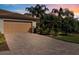 Beautiful exterior view with a two-car garage, tile roof, brick drive, and palm trees against a colorful sunset at 115 Babbling Brook Run, Bradenton, FL 34212