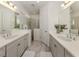 Bright bathroom with double sinks, framed mirrors, shower, and gray cabinetry at 18002 Franklin Park Ct, Venice, FL 34293
