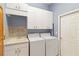 Well-lit laundry room with white cabinets, mosaic backsplash, utility sink, washer, and dryer for convenient chores at 201 Bayside Ct, Nokomis, FL 34275