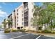 Condominium complex exterior featuring beige siding, a parking lot, tropical landscaping, and a blue sky at 3006 Caring Way # 304, Port Charlotte, FL 33952