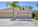A tan home with a tile roof and a three-car garage surrounded by lush landscaping at 5641 Hidden Oak Ct, North Port, FL 34287