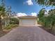 A home's two-car garage features a red brick drive and lush tropical landscaping at 13150 Huerta St, Venice, FL 34293